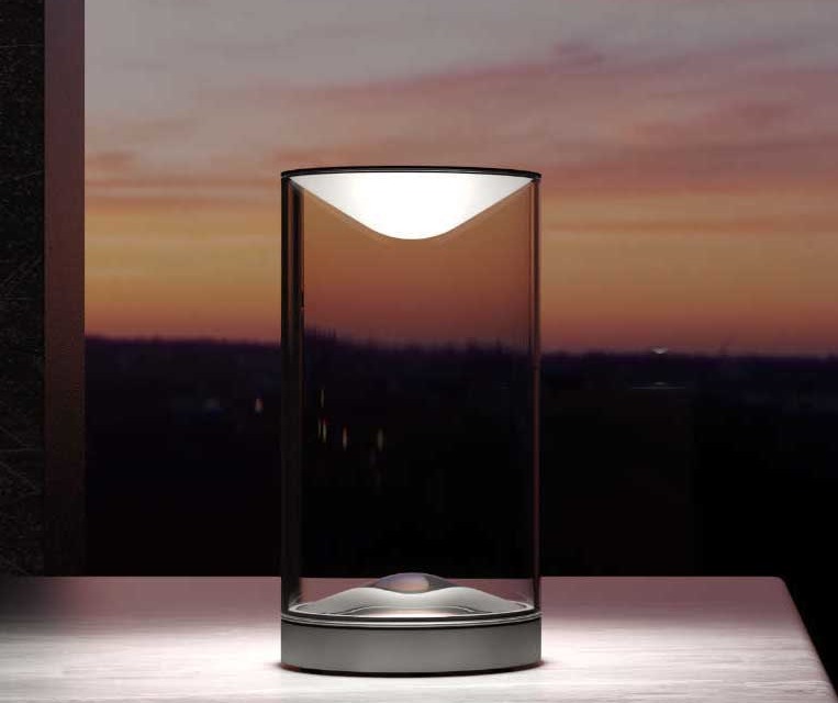 Cette lampe Eva&Eve LED de table Lumina diffuse une lumière indirecte dans un cylindre en verre transparent avec une structure en aluminium.